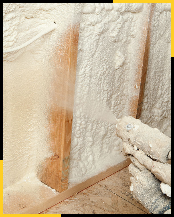 Construction worker spraying expandable foam insulation between wall studs
